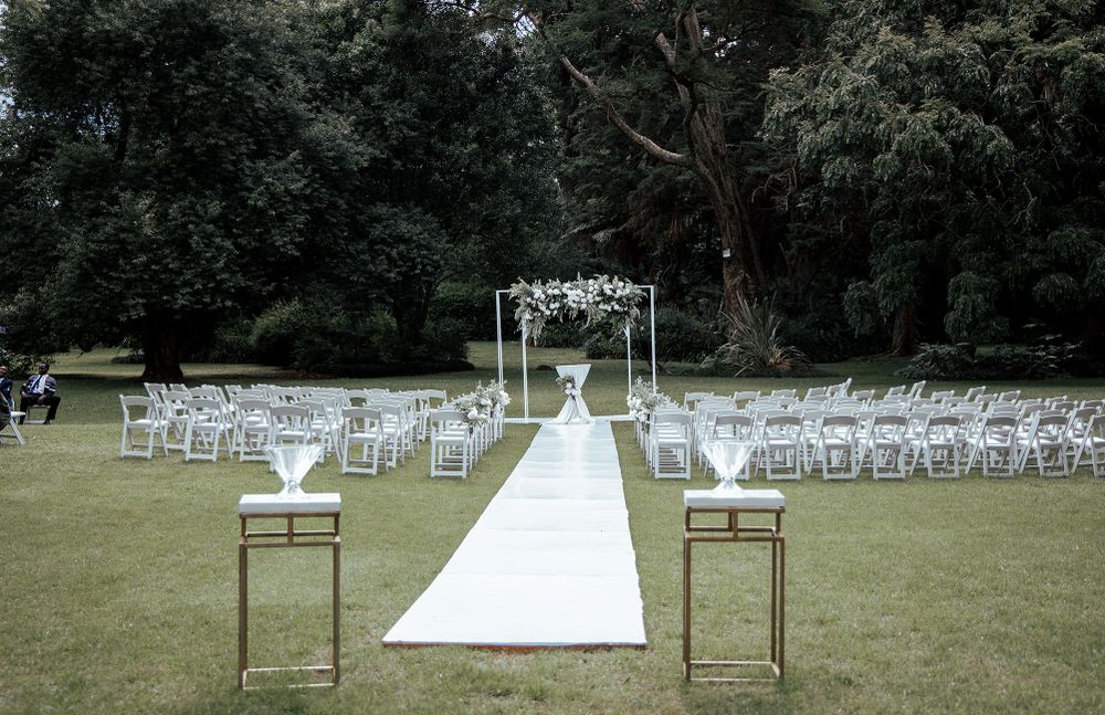 Outdoor wedding ceremony setup with white chairs and aisle runner leading to decorated arch.