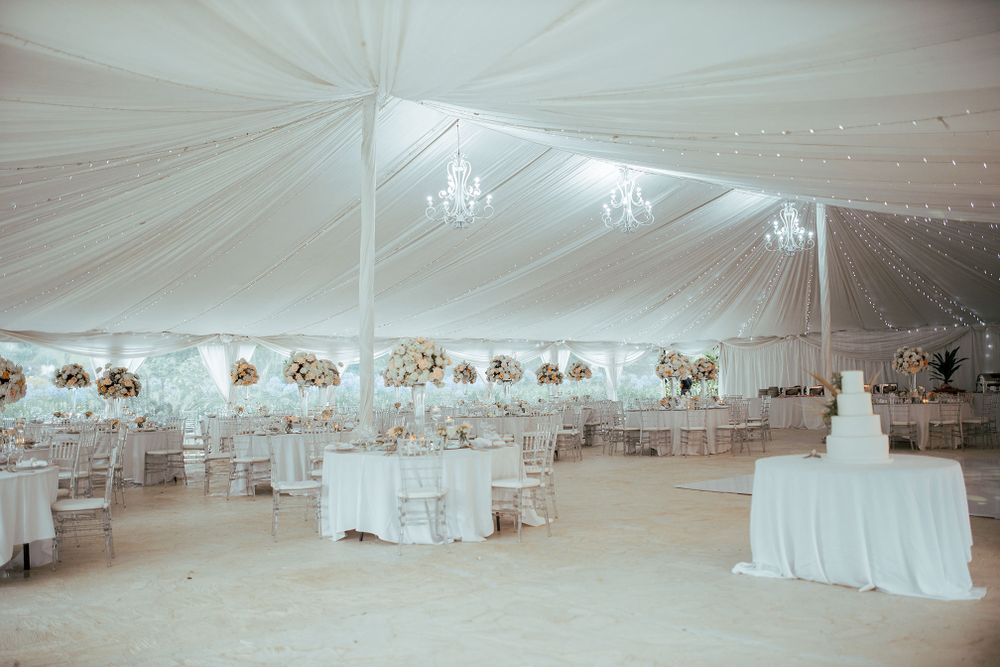 White wedding reception tent with chandeliers and round tables set for dining.