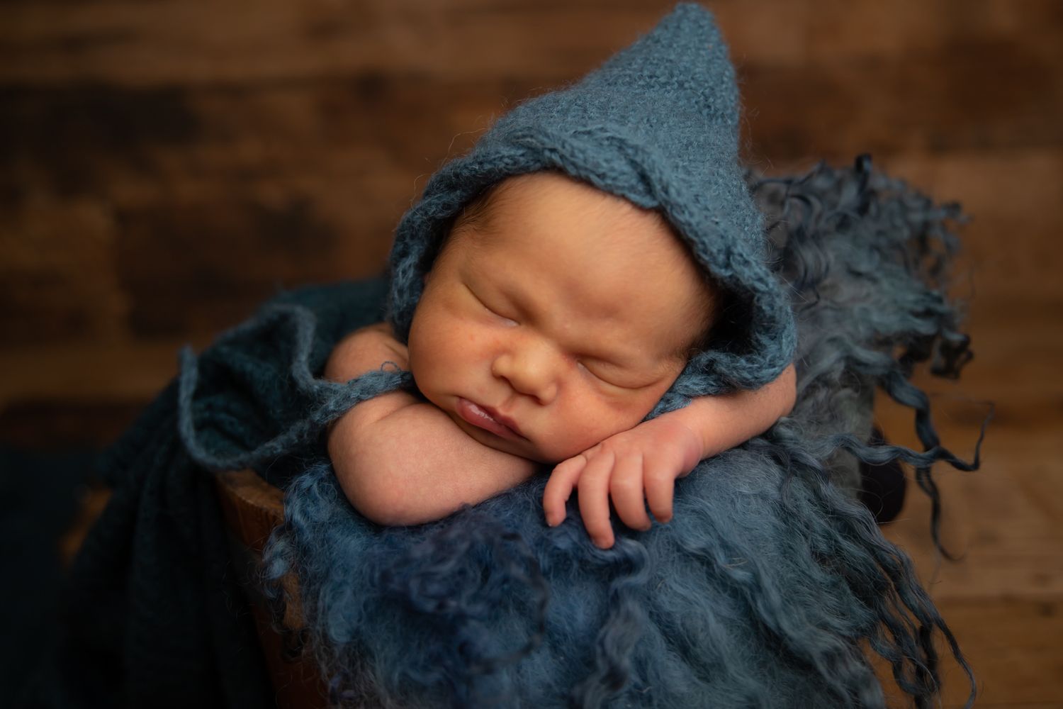 Sleeping newborn wrapped in soft blue knitted wrap on dark background.