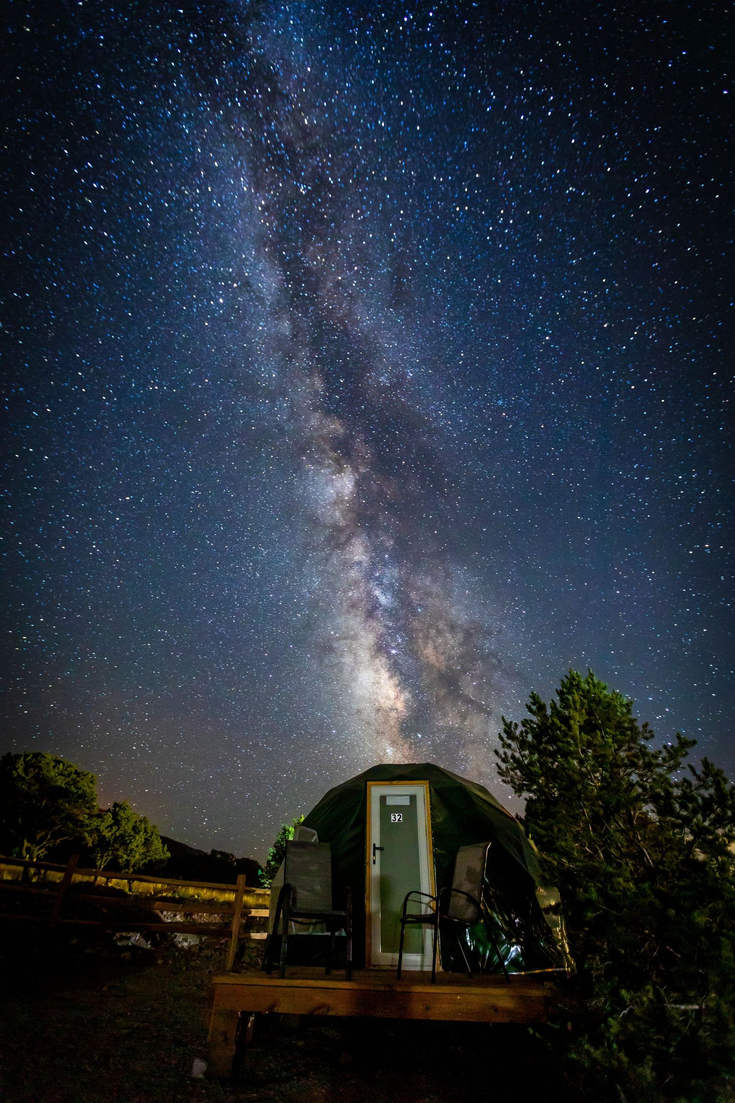 Milky Way galaxy stretches across the night sky above silhouetted farm buildings.