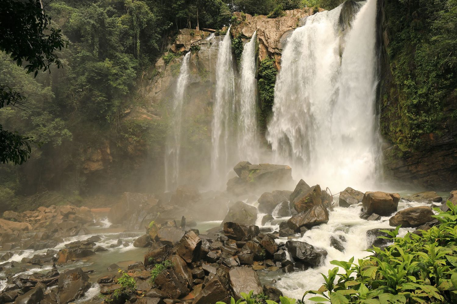 Majestic waterfall cascades over rocky cliffs in a lush tropical forest setting.