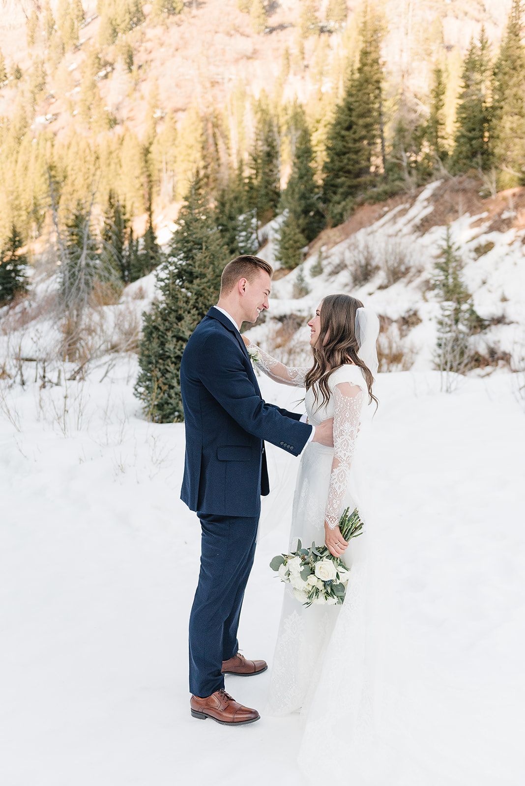 Wedding couple shares an intimate moment in a snowy mountain setting with golden cliffs behind.