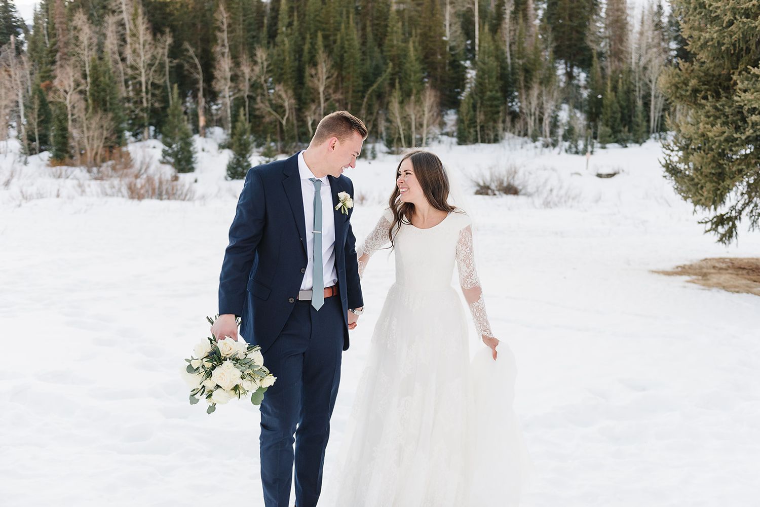 A winter wedding portrait with fresh snow and evergreen trees in the mountain landscape.