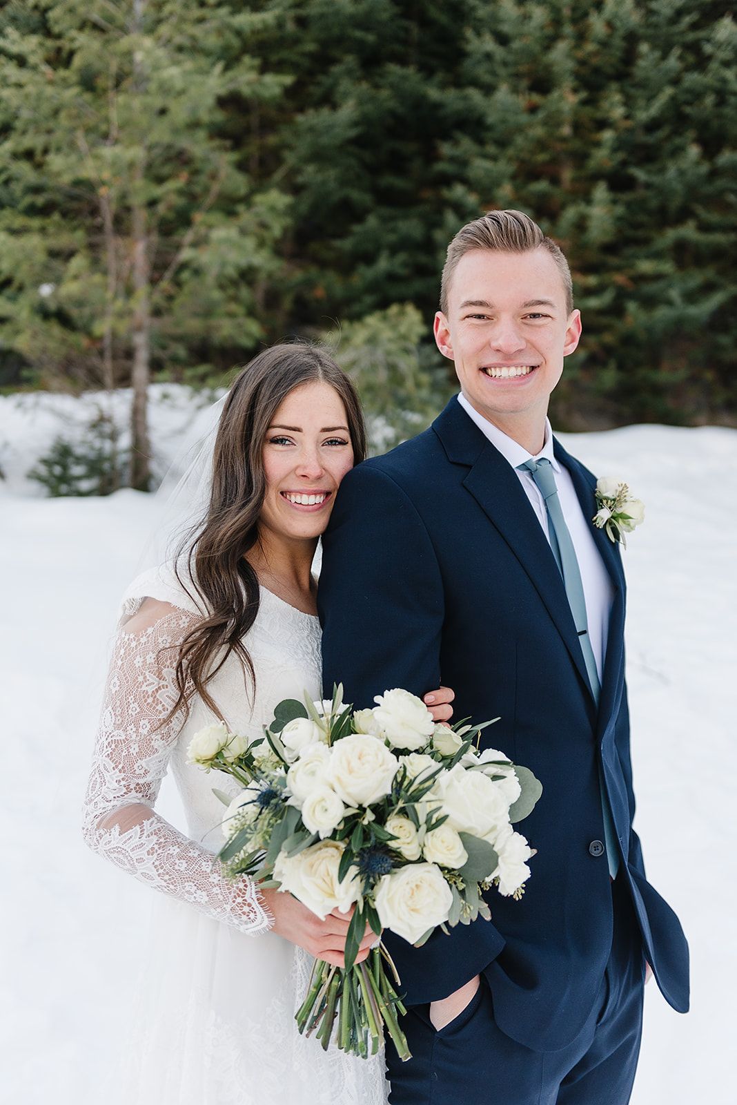 Bright winter wedding portrait featuring a white bouquet and snow-covered mountain landscape.