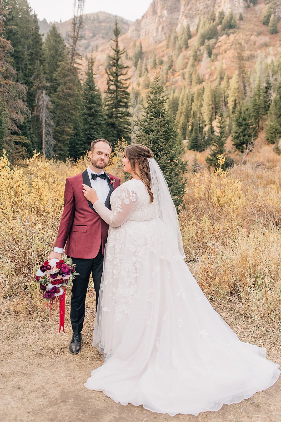 Wedding portrait in autumn mountains with burgundy attire and dramatic mountain backdrop.