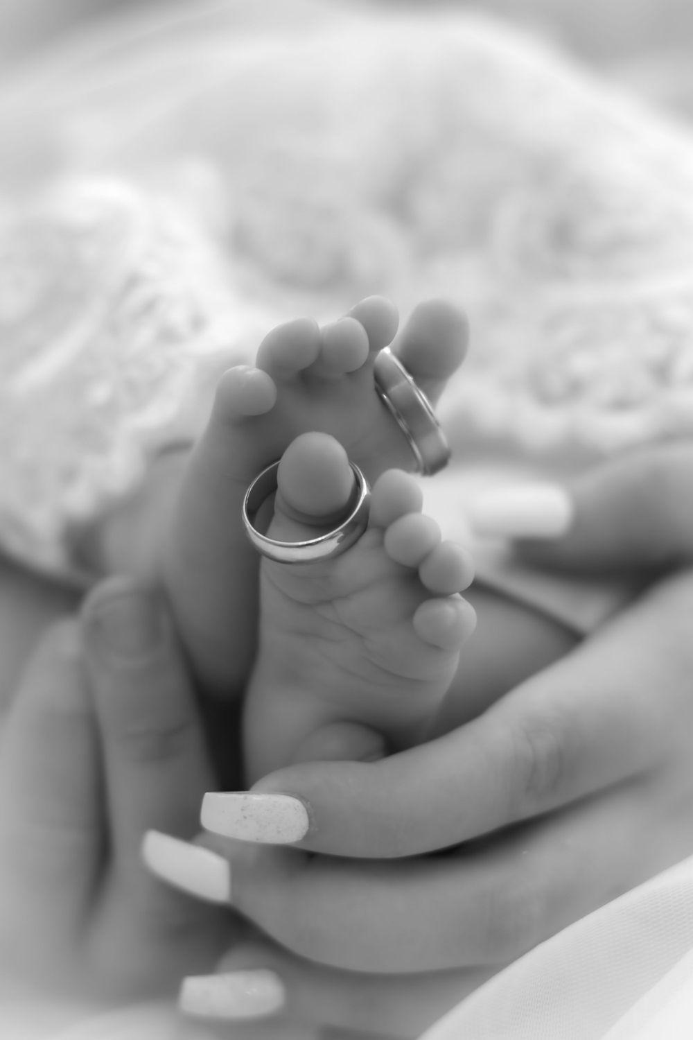 Close up black and white photo of a baby's foot with a wedding ring balanced on the tiny toes.