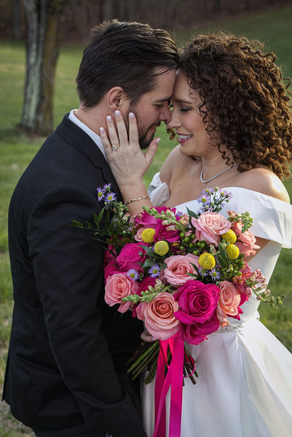 A wedding couple shares an intimate moment with a vibrant pink and coral bouquet.
