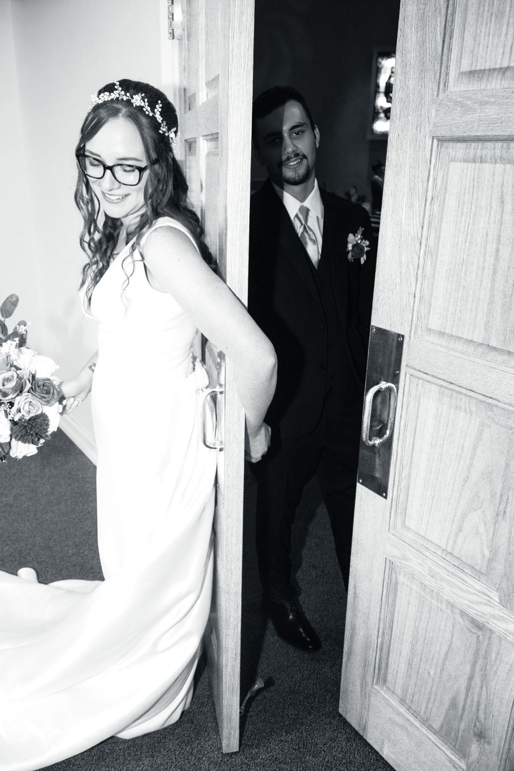 Black and white photo of a playful wedding moment through a doorway.