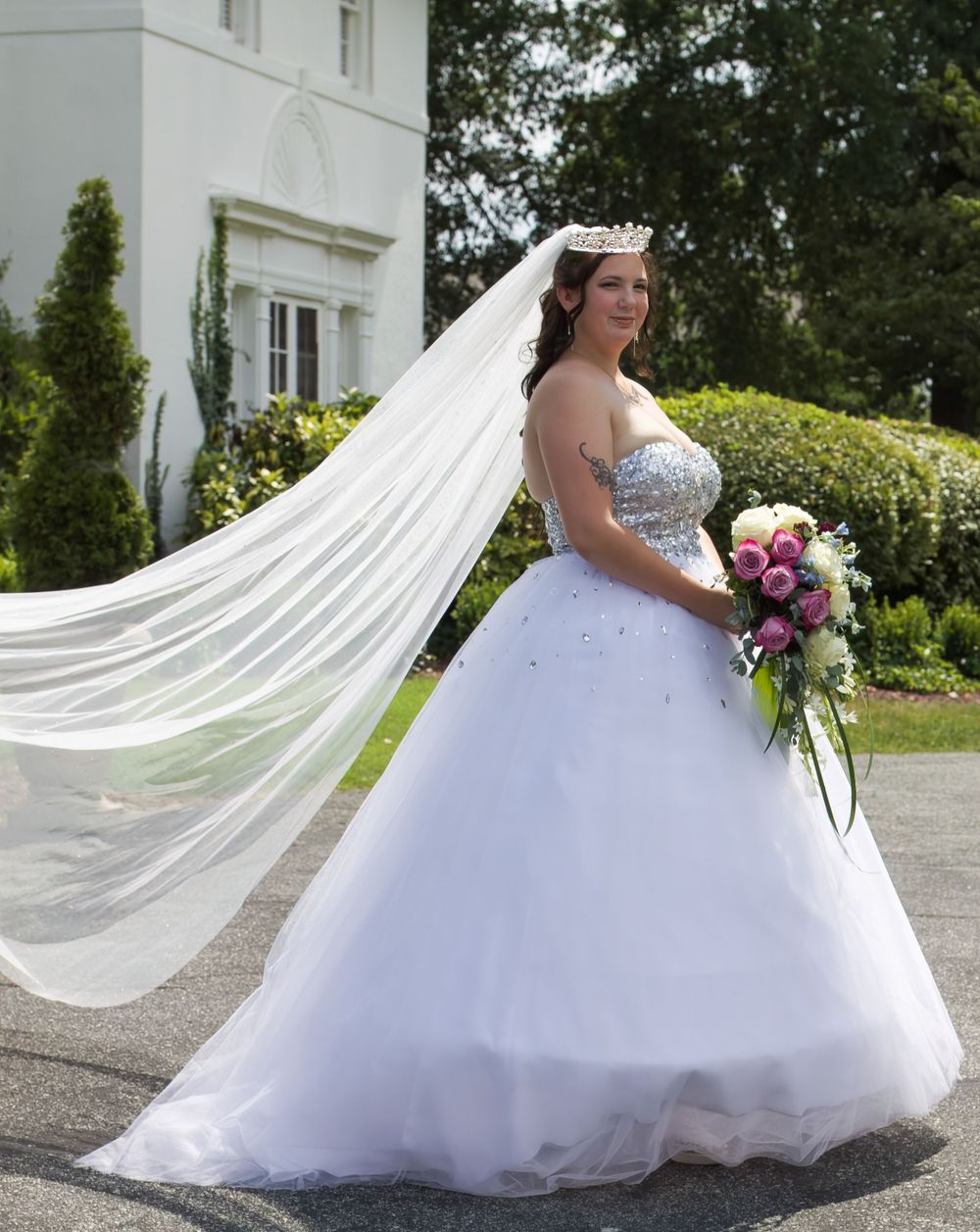 A bride in a stunning ball gown with her flowing veil and pink bouquet.