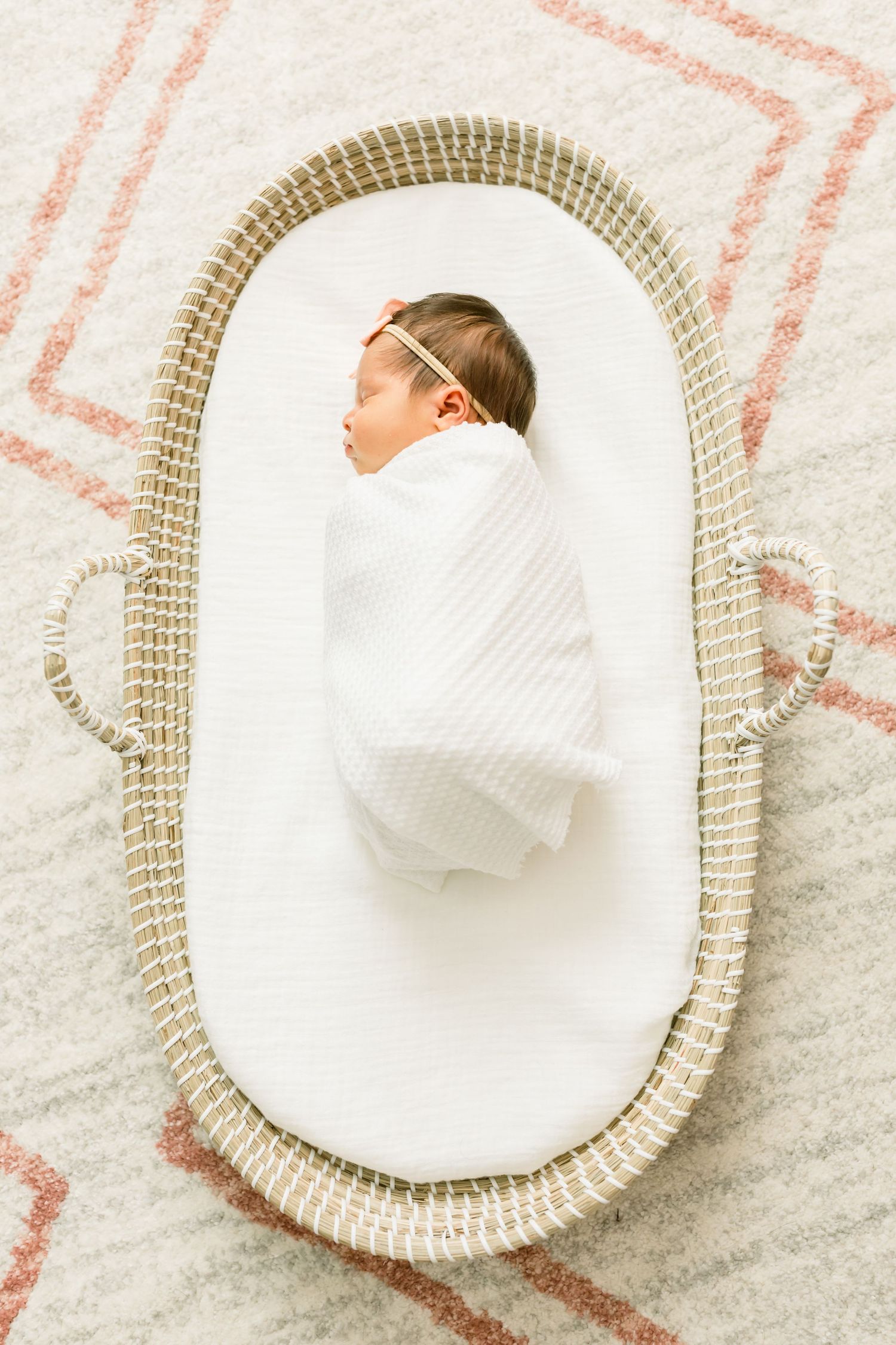 Peaceful newborn wrapped in white blanket sleeping in woven moses basket.
