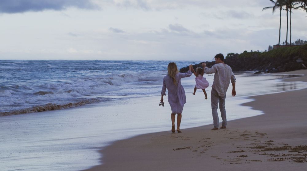 Family photography. Couple swing their daughter in the air in beach pose photography, natural. Family photography Dorset