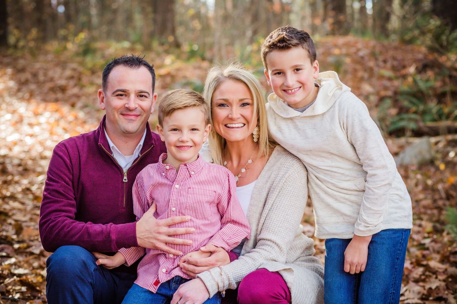 A family of four poses together outdoors during an autumn photoshoot with fallen leaves in the background.