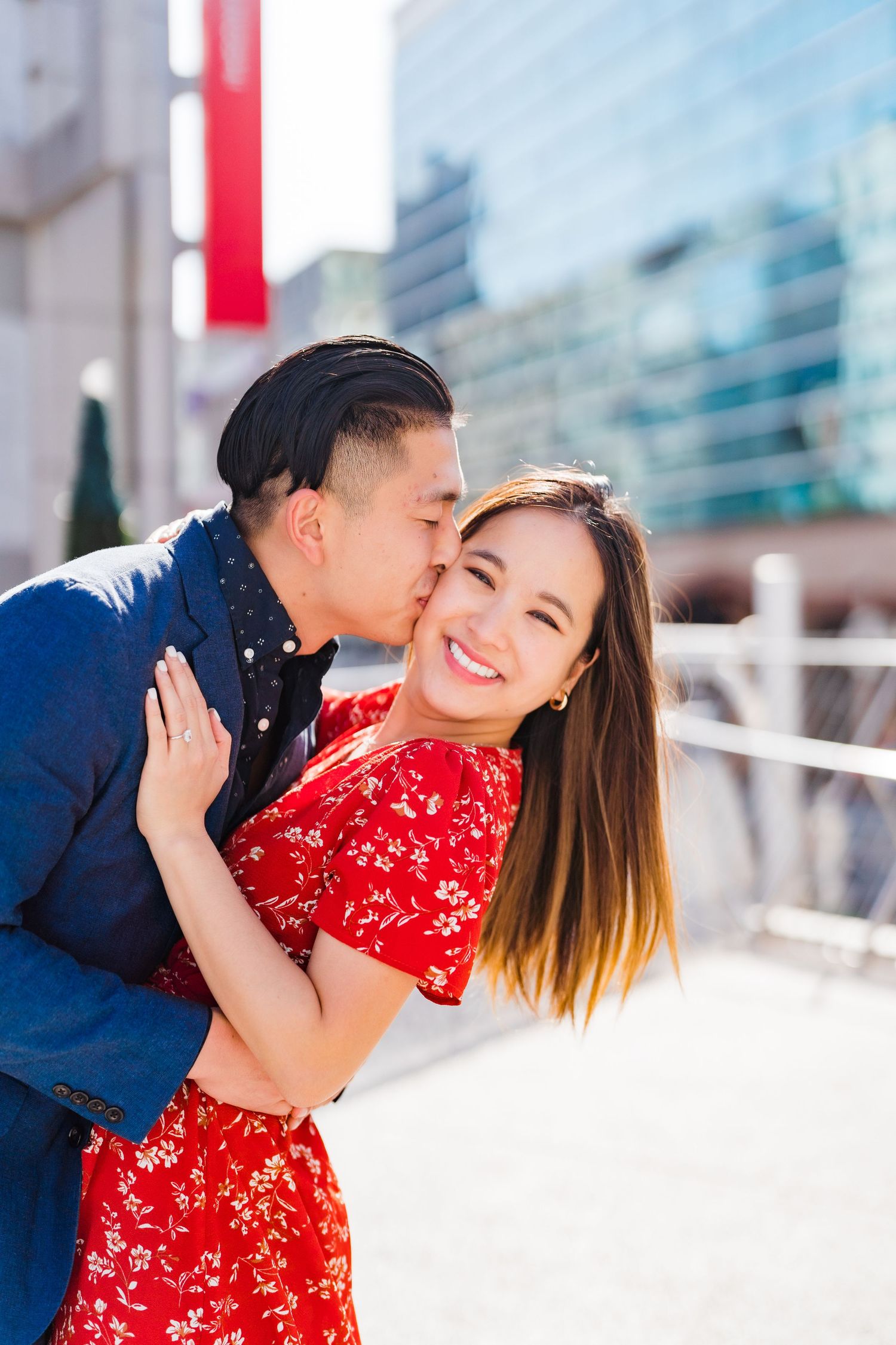 Couple sharing sweet moment outdoors against urban backdrop with modern buildings.