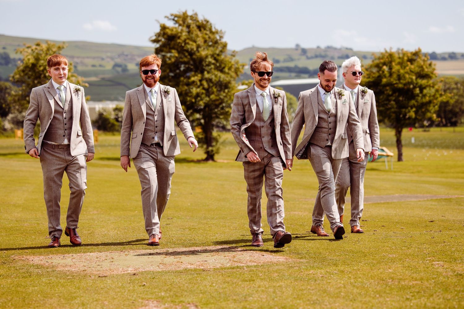 Groomsmen walking together across lawn in coordinated gray suits.
