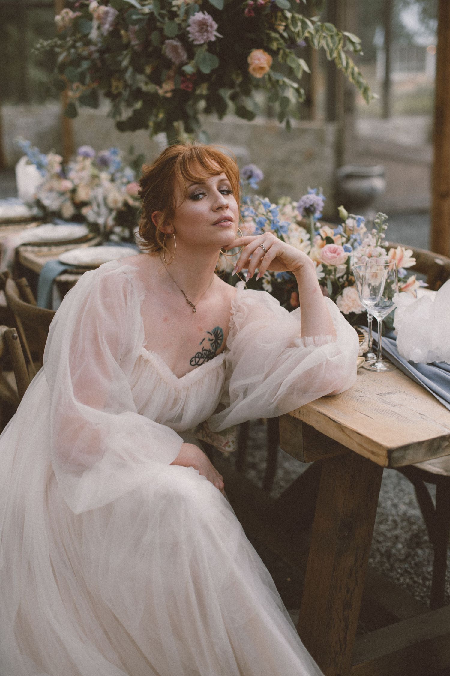 Ethereal bridal portrait with soft pink tulle gown and floral arrangements in a greenhouse setting.
