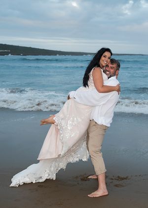 A romantic beach wedding photo with couple embracing against ocean backdrop.