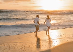 Two silhouettes running together on beach at golden hour sunset.
