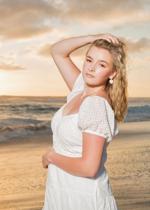 A portrait of a woman in white eyelet dress posing on beach at sunset.