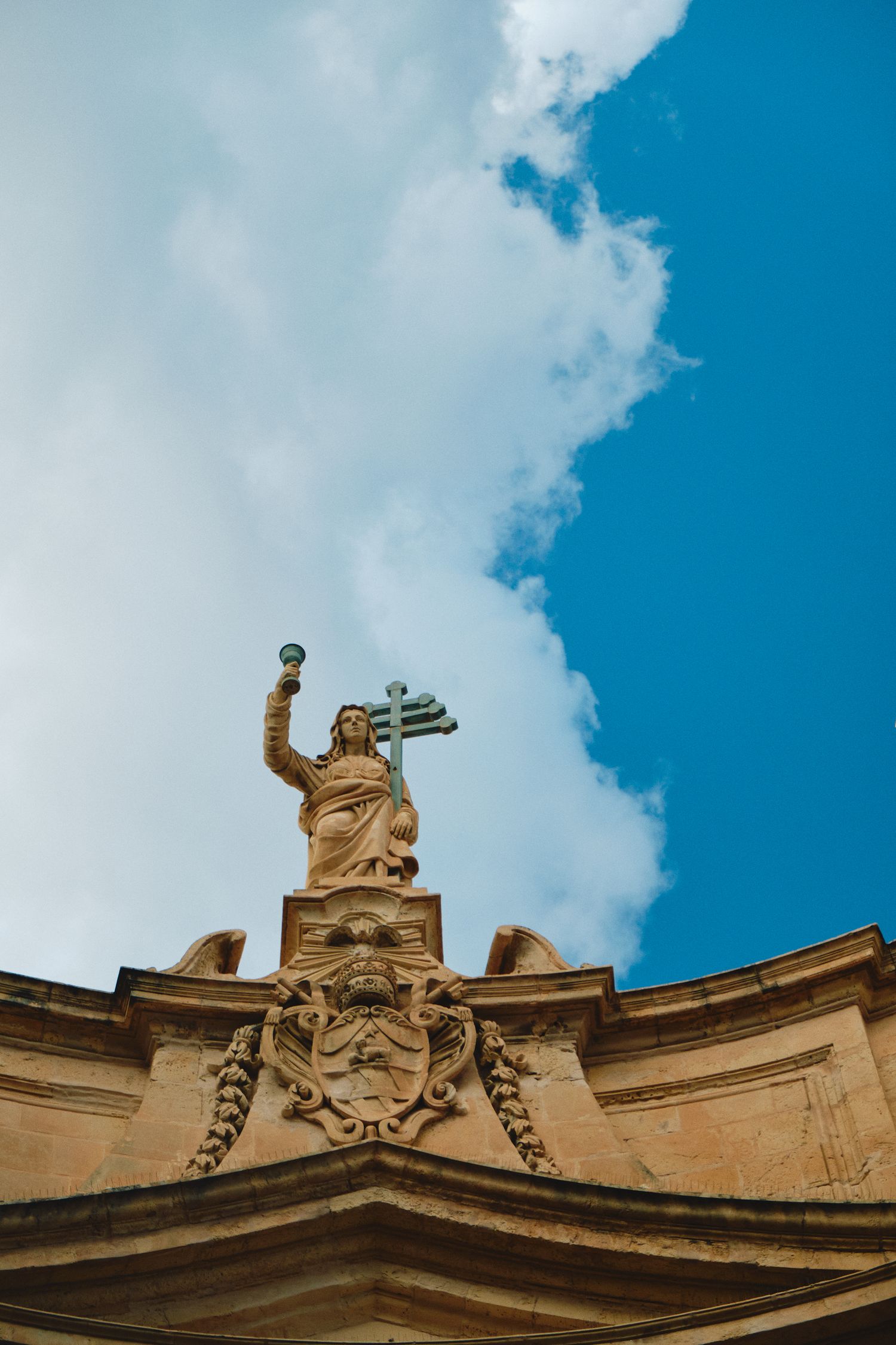 A golden religious statue stands atop an ornate baroque church facade against a blue sky.