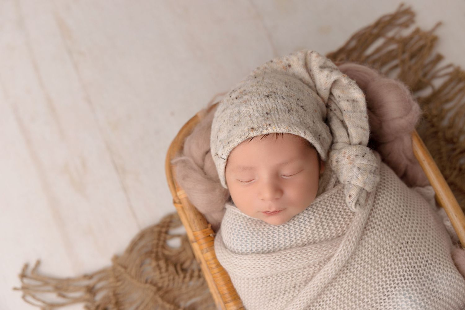 Sleeping newborn in knitted outfit on woven textured backdrop.
