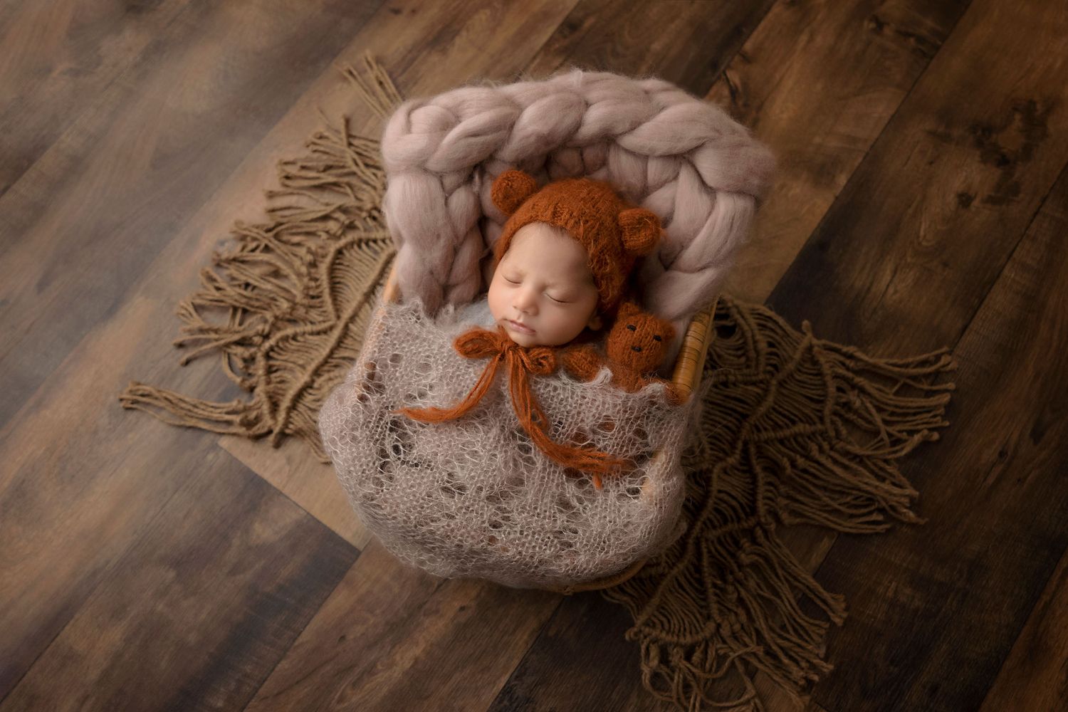 Newborn with red hair sleeping peacefully in knitted nest surrounded by neutral tones.