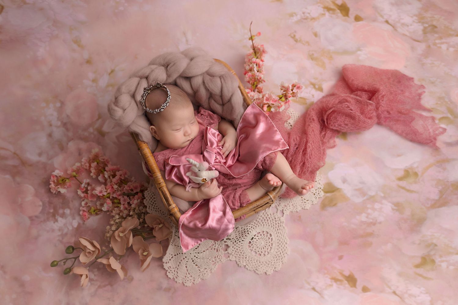 Sleeping newborn on pink backdrop with floral accents and lace details.