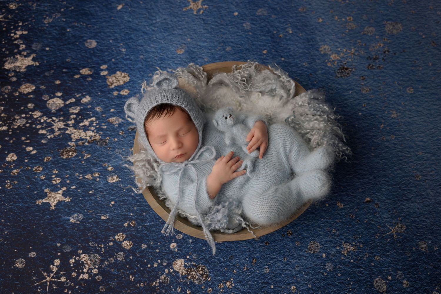 Sleeping baby in bonnet on blue surface with white fluffy decorations.