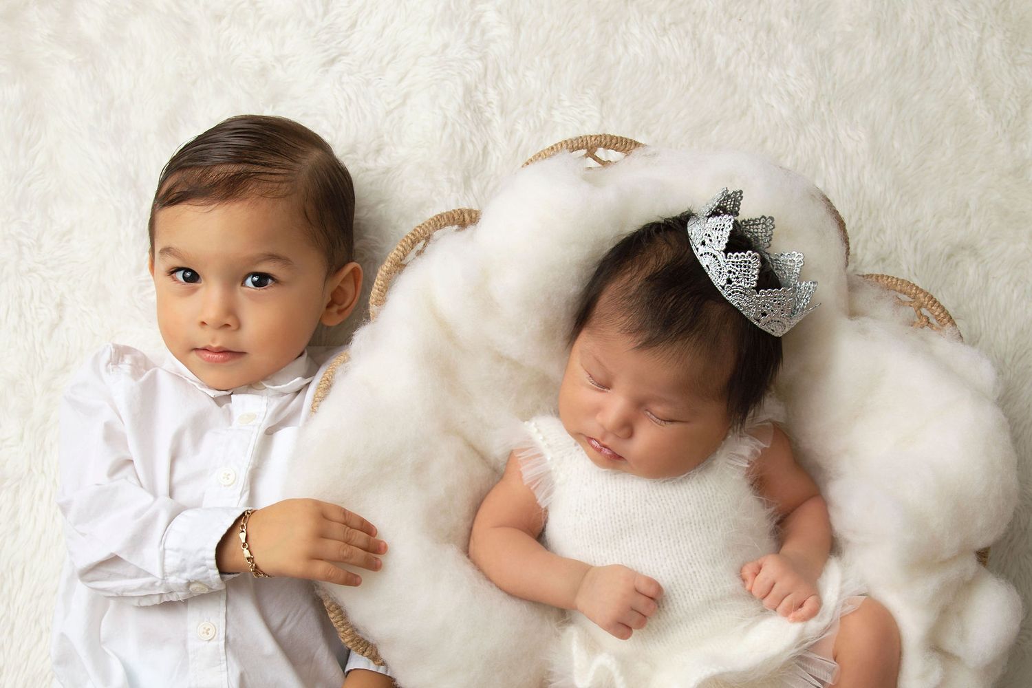 Two young children in white outfits posed together on a light neutral background.