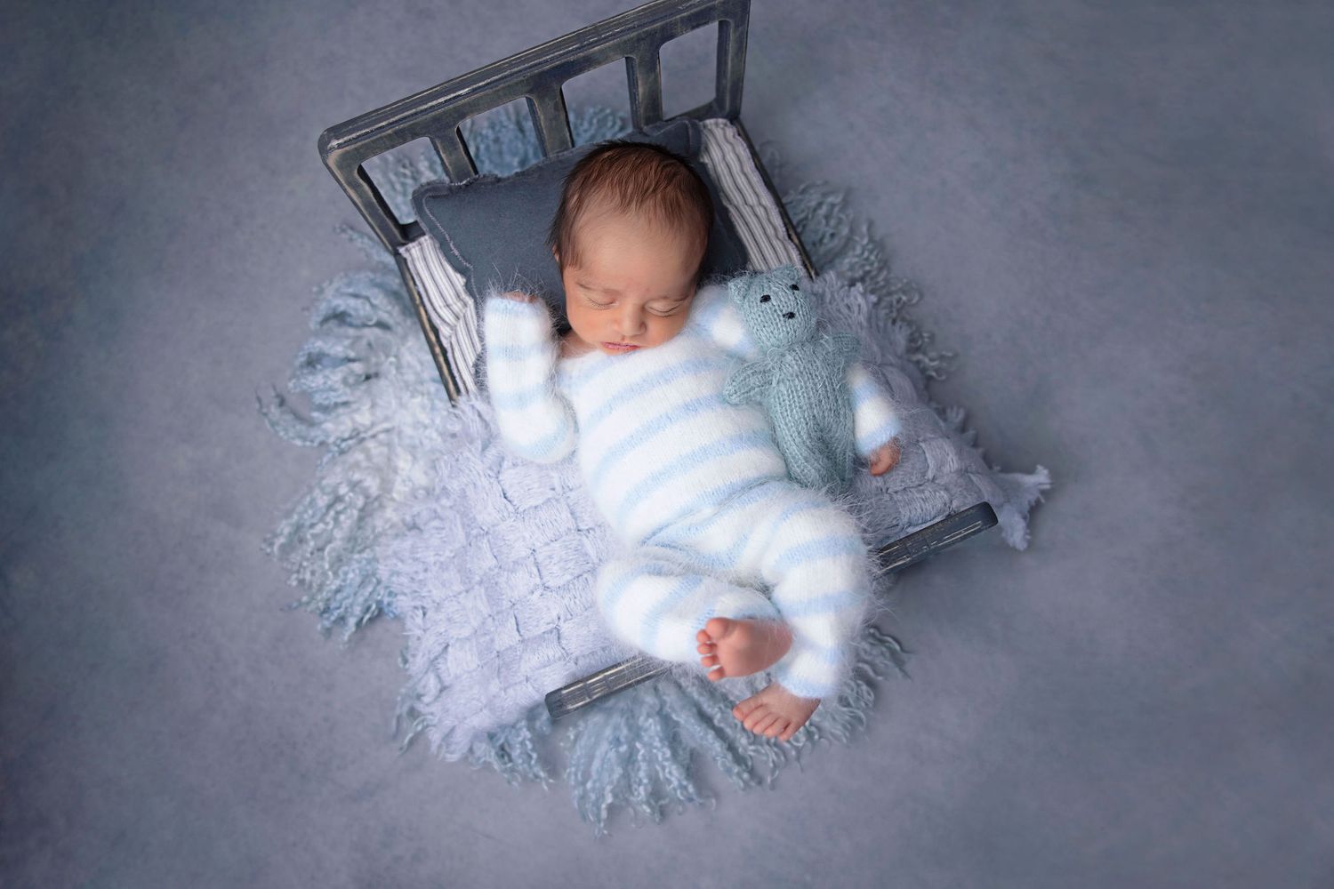 Newborn baby sleeping in miniature bed with white and blue winter theme decor.