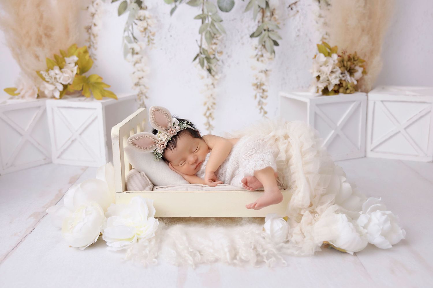 Sleeping baby on white couch with floral backdrop and delicate decor elements.