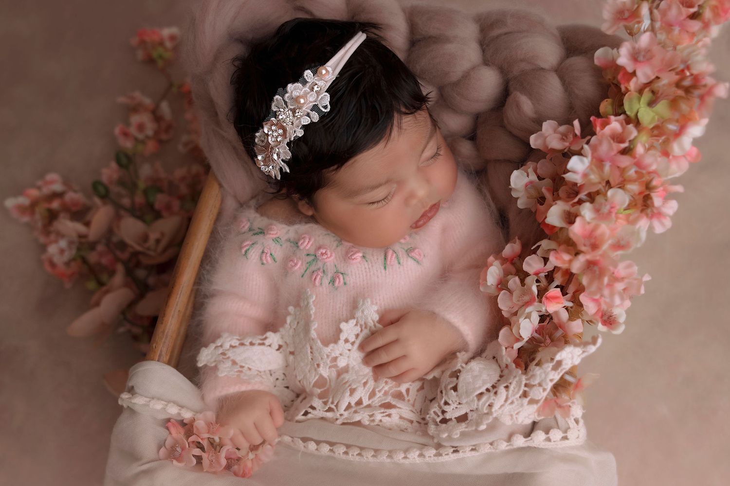 Dreamy newborn portrait with cherry blossoms and lace details in soft pink tones.