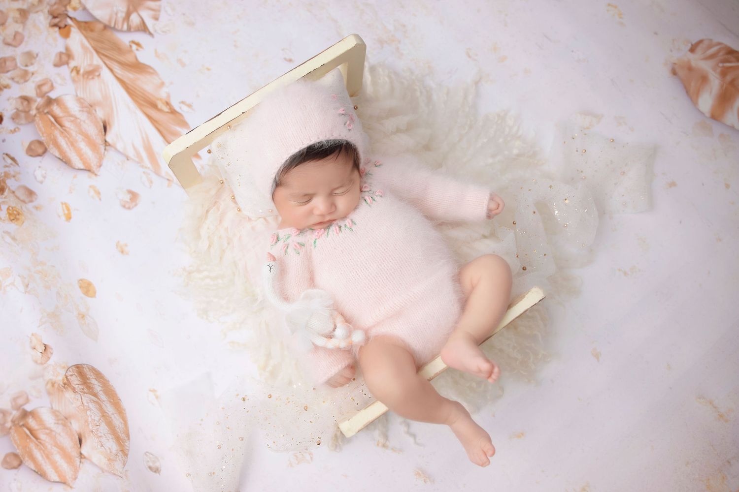 Sleeping newborn on white fluffy rug with peach-colored backdrop and wooden props.