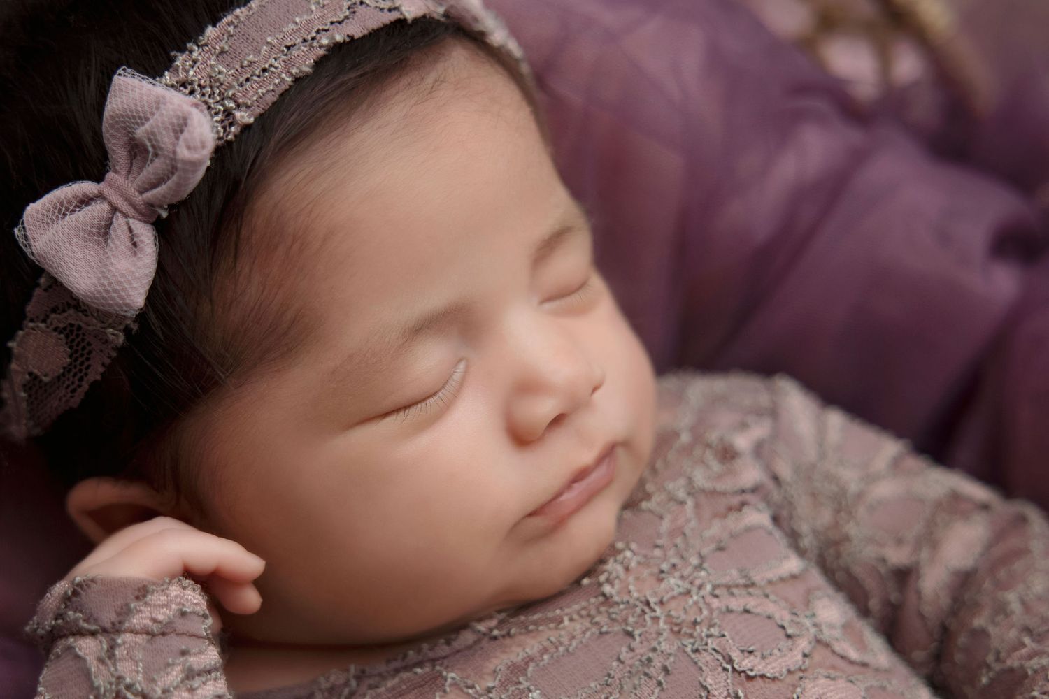 Sleeping newborn in purple lace dress with matching bow headband.