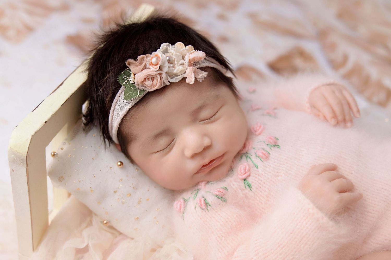 Peaceful sleeping baby wearing floral headband against soft pink background.