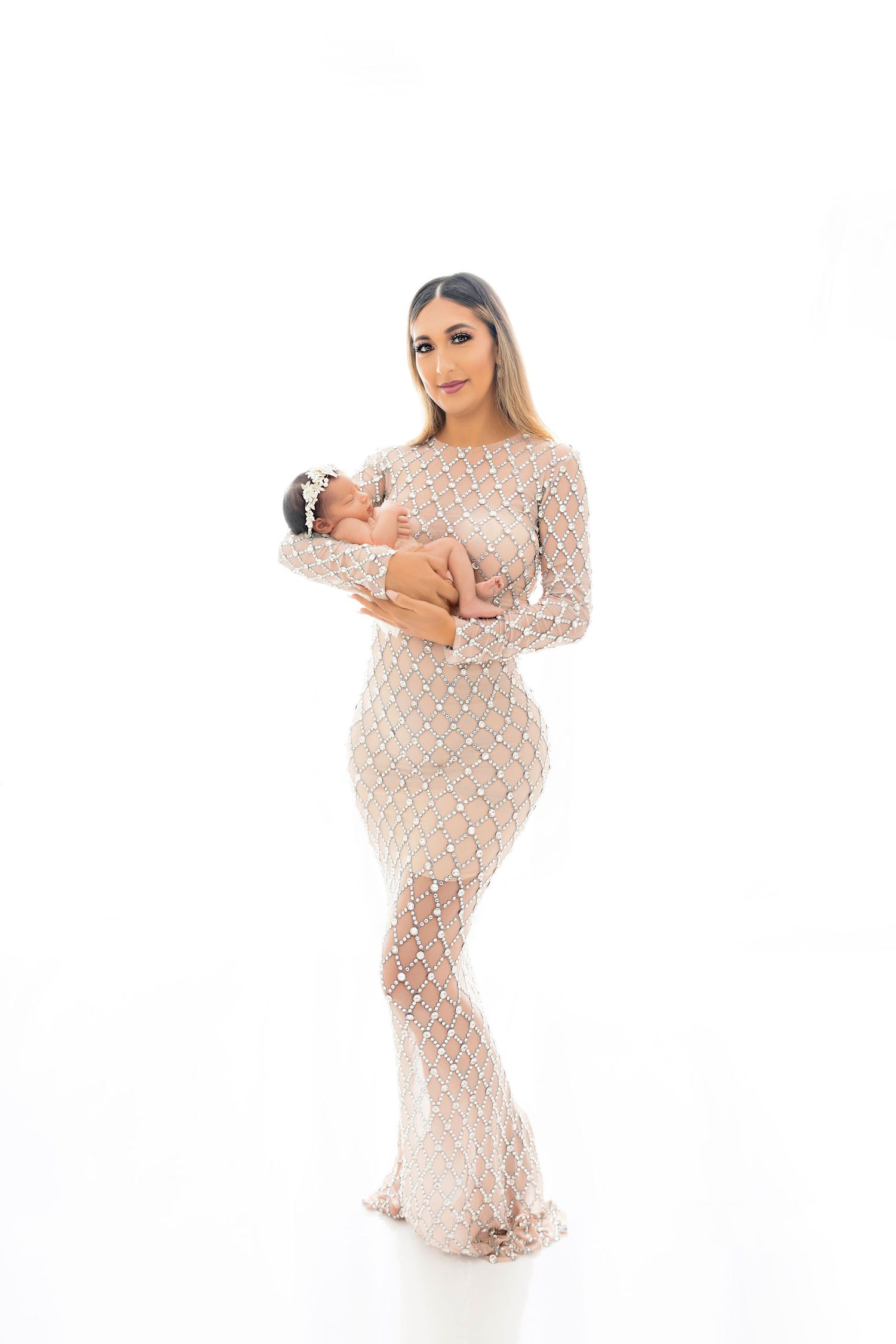 Mother in beaded gown holding newborn against white background.
