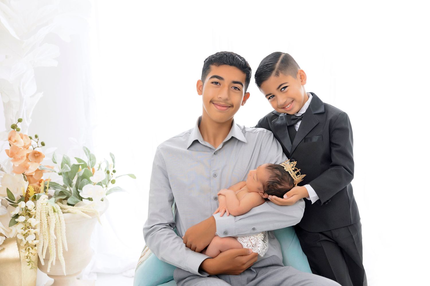 Two people with newborn in studio setting with floral decorations.