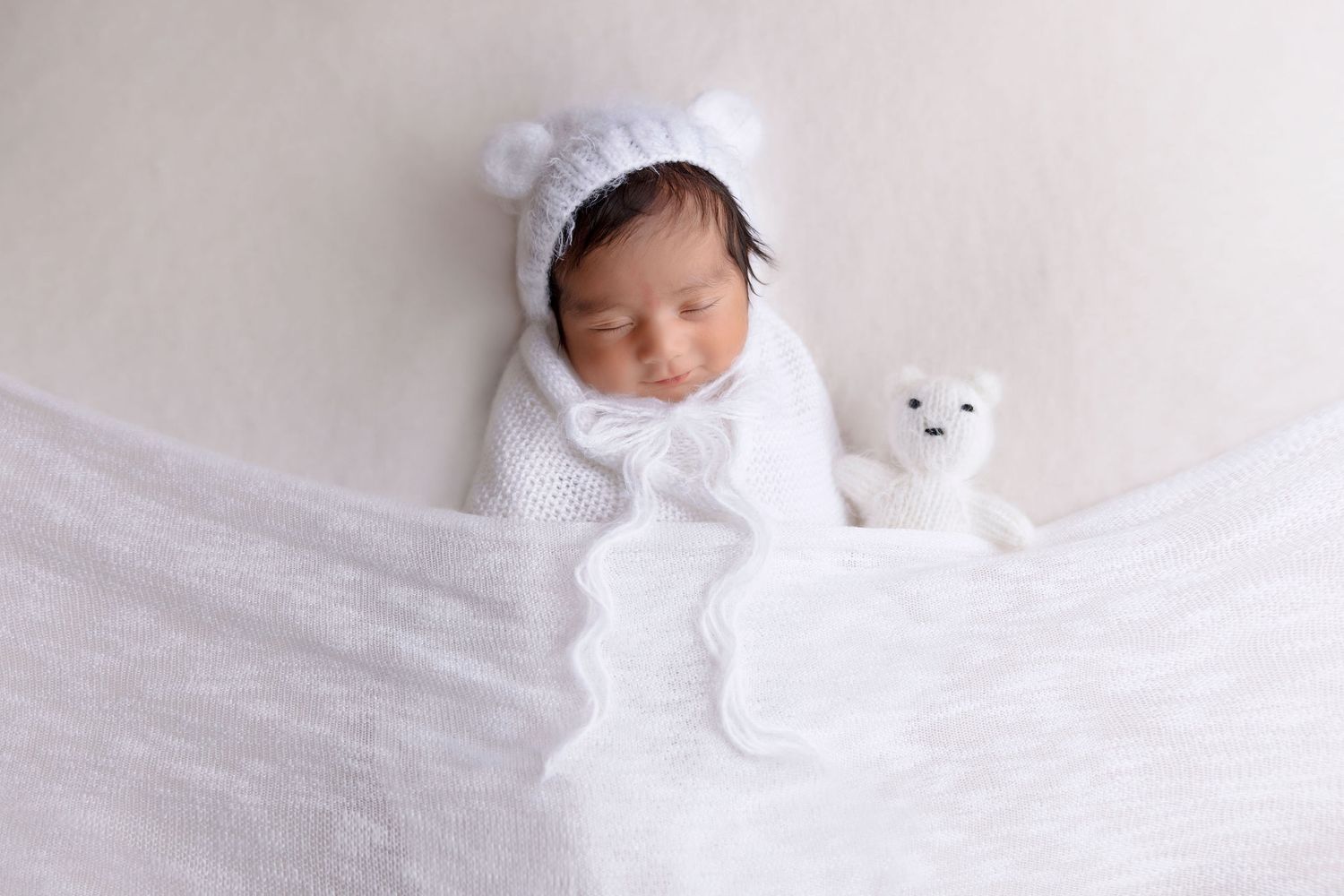 Sleeping baby in white bear outfit with small plush toy.