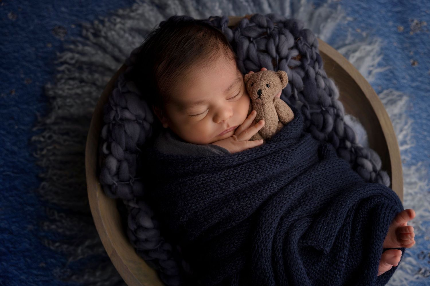 Peaceful sleeping baby wrapped in navy knitted blanket on textured surface.