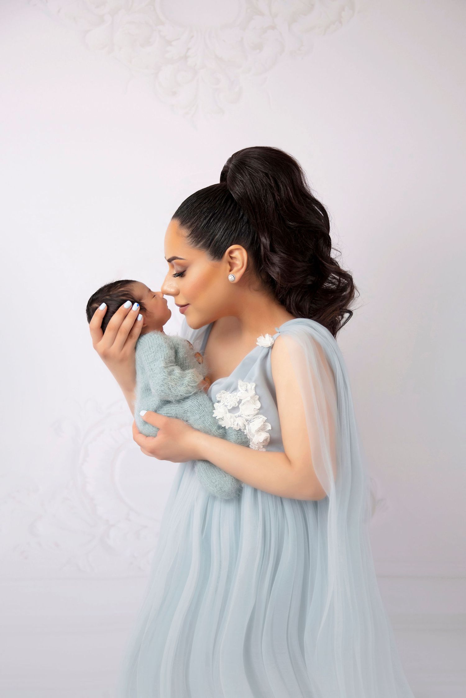 Woman in flowing blue dress holding small bundle with tender expression.