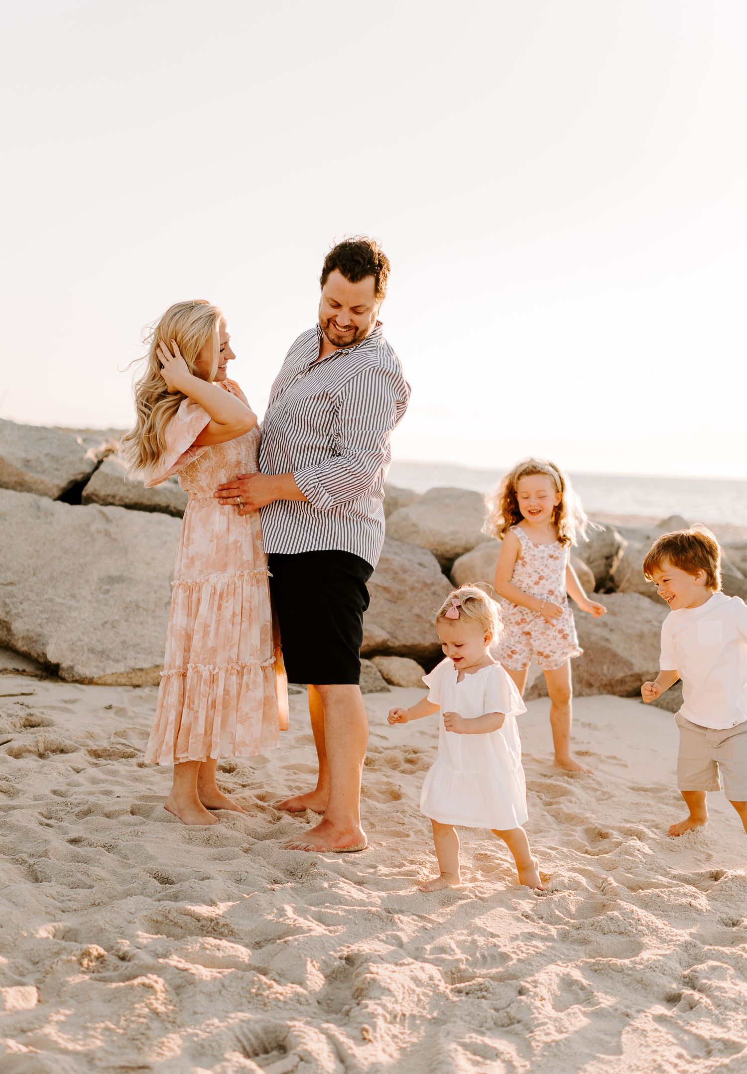 Family enjoying sunset together on sandy beach with children playing.