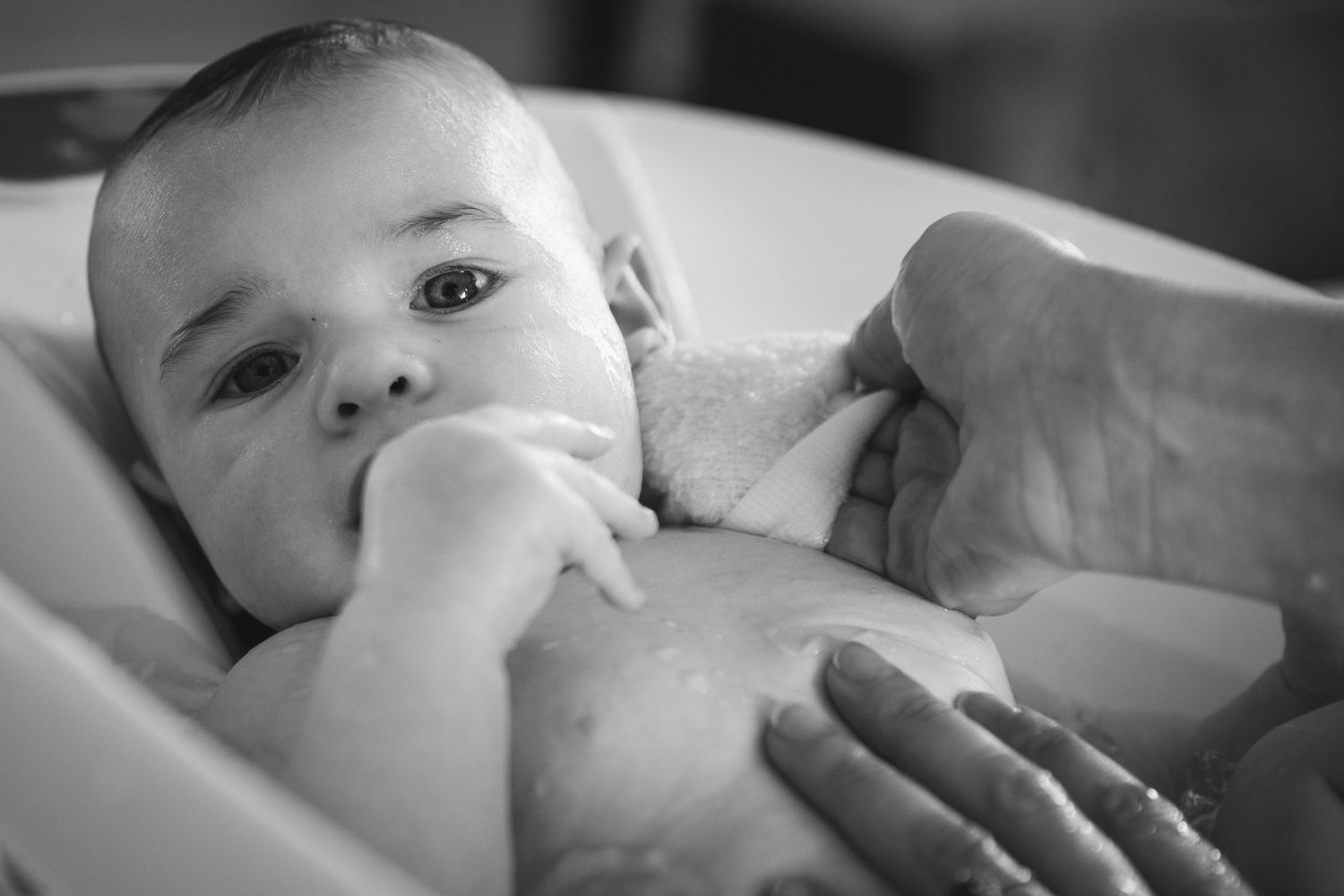 Black and white portrait of baby resting hand near face while lying down.