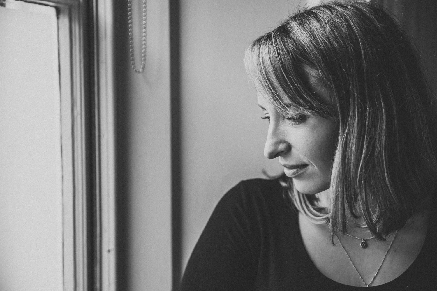 Black and white portrait of person gazing thoughtfully out window.