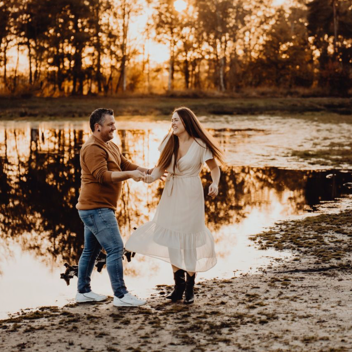 Couple splashing in water during golden hour near pond.