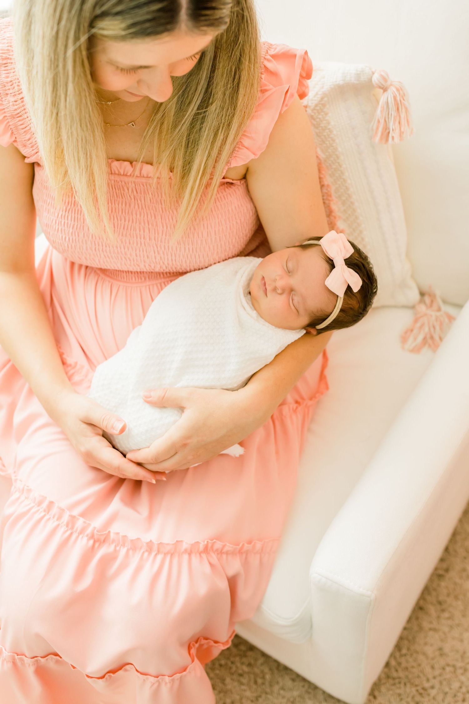 Newborn baby wearing white bow sleeps peacefully in mother's arms.