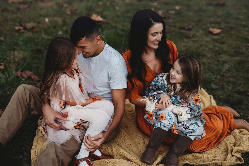 Family relaxing together on blanket outdoors during casual lifestyle session.