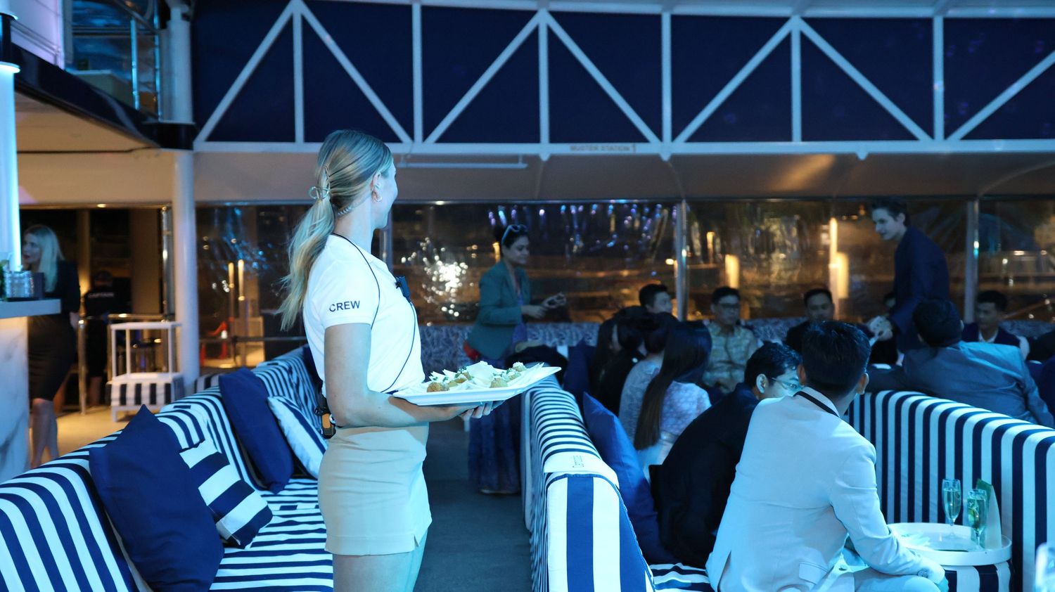 A server in white uniform tends to guests at a dimly lit venue with blue accent lighting.
