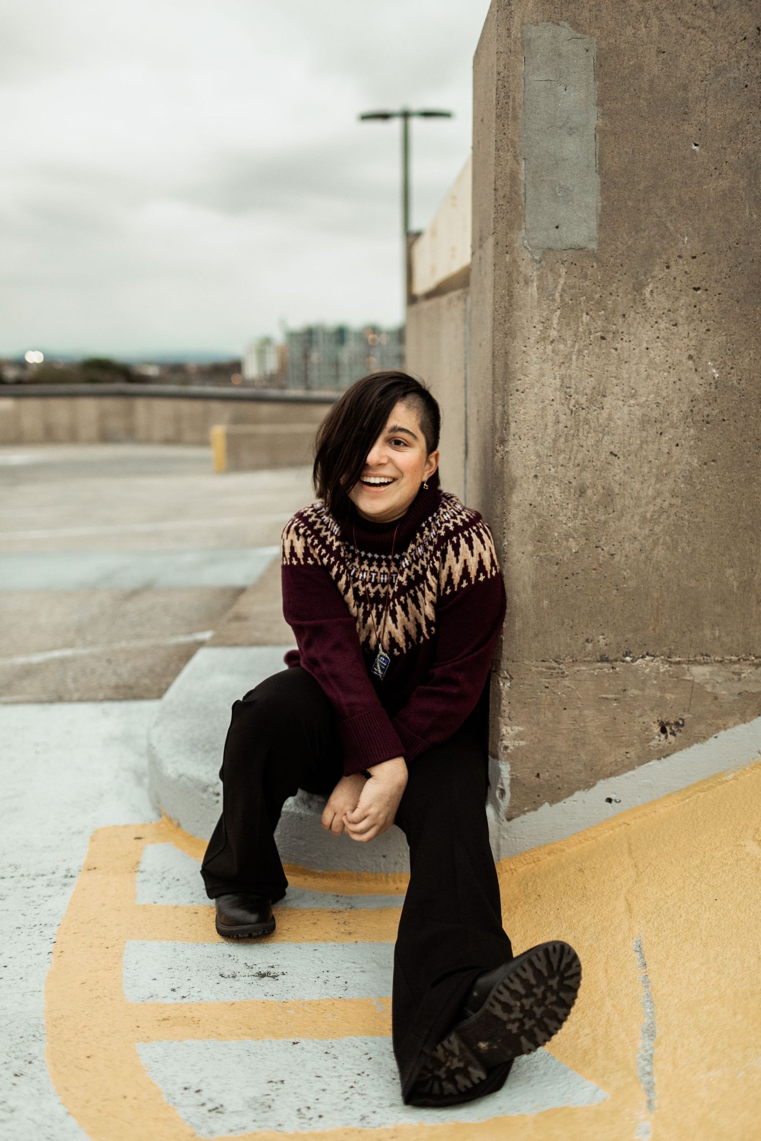 Person wearing patterned sweater sitting and laughing in parking garage.