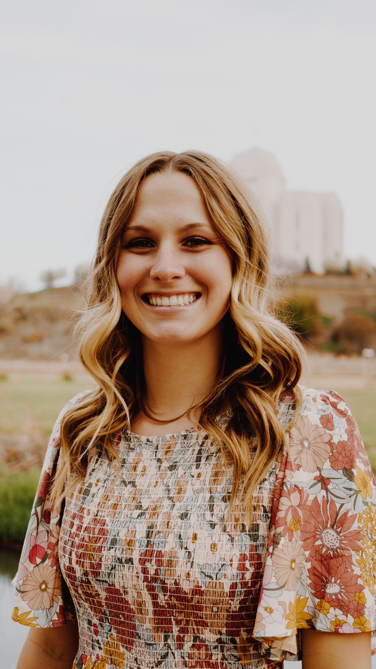 A portrait of a person smiling, captured in natural light, with a simple background.