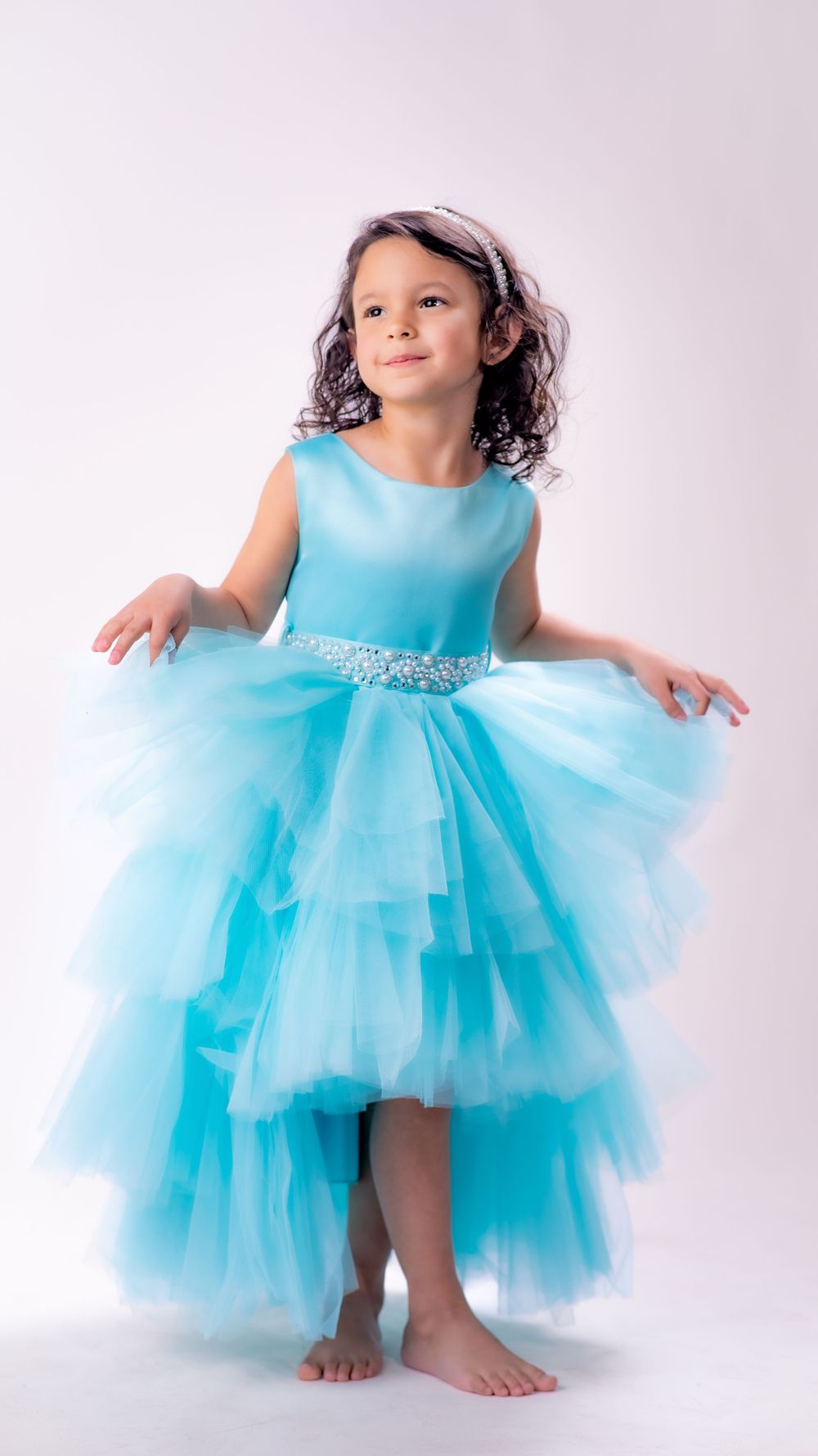 Young girl poses gracefully in a stunning hi-low turquoise tulle gown with jeweled waistband.