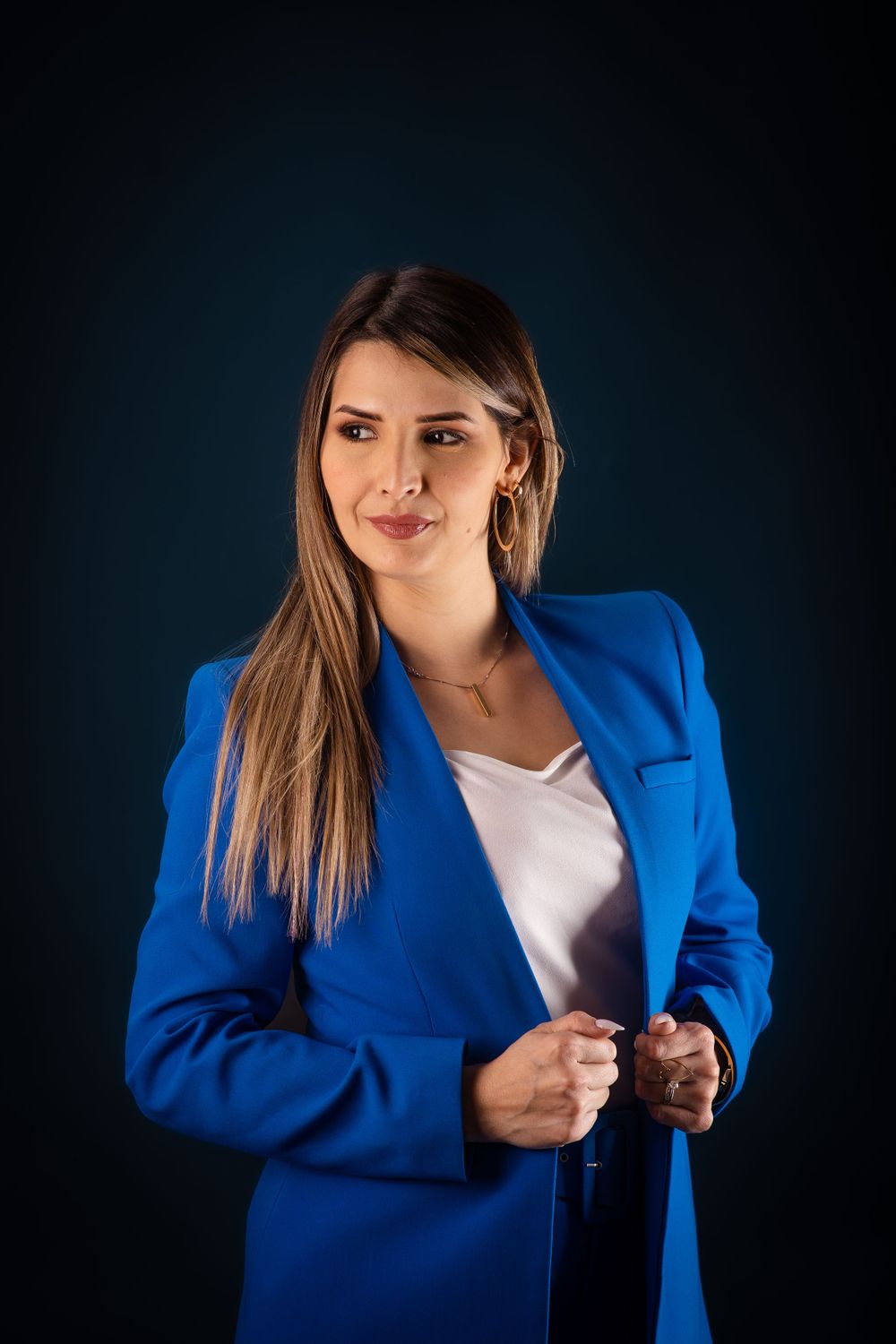 Professional woman in blue blazer and white top posing confidently against dark background.